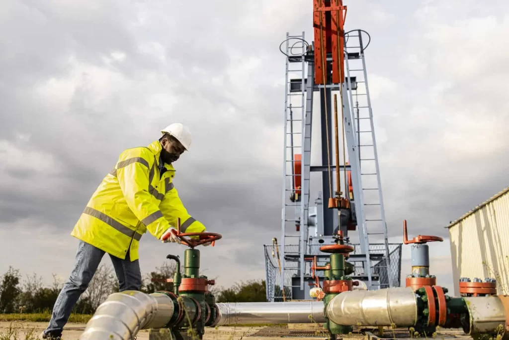 oil field worker closing industrial valve by oil rig controlling production